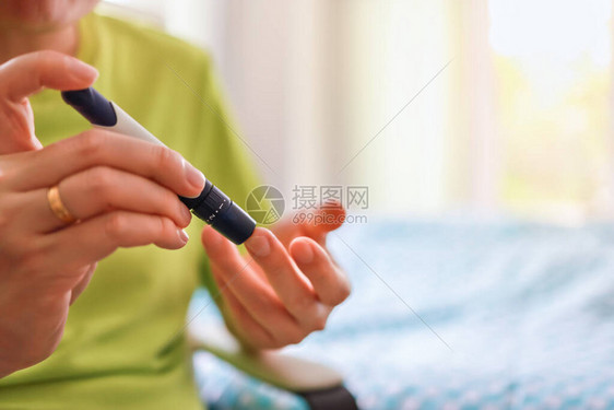 早上用手指上的柳叶刀在卧室里用血糖仪检查血糖水平的人手的特写用作医学糖尿病血糖保图片