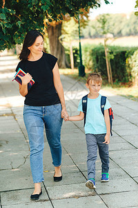 妈带孩子上学在学校的第一天母亲带领一个小学生上一年级小学的家长和学生齐头并进背着包背景图片