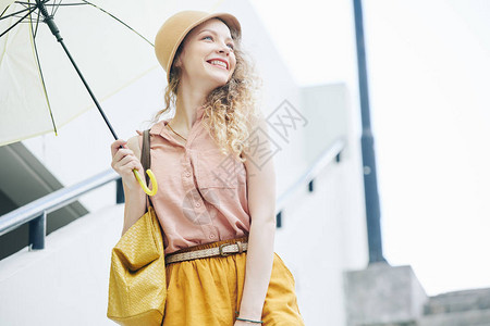 带着雨天伞在户外散步的戴着帽子的迷人女士图片