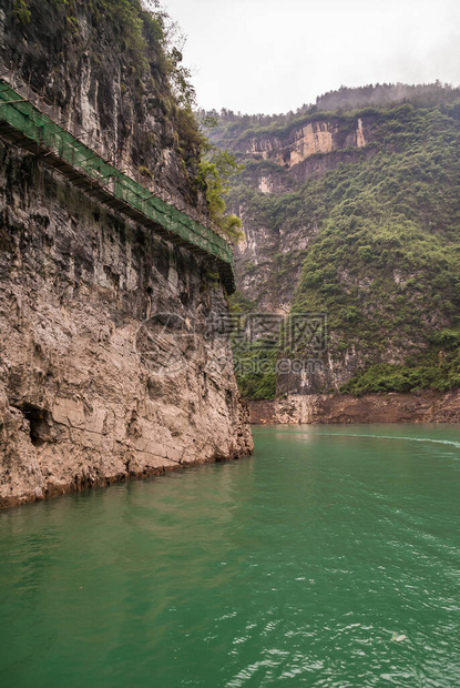 大宁河上的大雾或迷雾峡谷在翠绿的水面上的棕黑色裸露悬崖上悬挂着绿色防护栅栏的木板图片