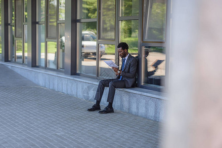 集中的非洲裔美国商人坐在办公楼的栏杆上阅读报纸图片