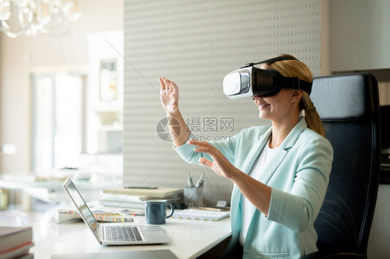 戴着VR眼镜的年轻女员工坐在办公室的办公桌旁图片
