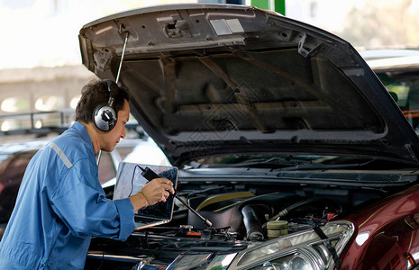 身穿蓝色制服的亚洲汽车机械师使用电子工具检查车库引擎盖附图片