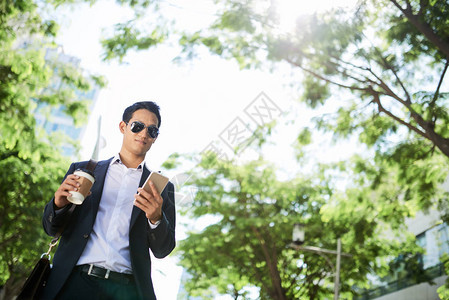 年青的太阳眼镜商人在匆忙上班时检查他的电话和喝咖啡图片