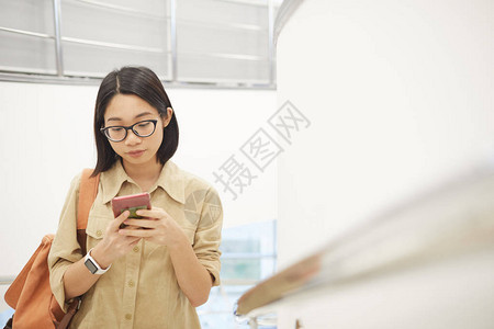 现代大学室内楼梯上使用智能手机的年轻亚洲女腰部肖图片