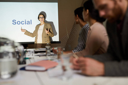 内容自信的女演讲者在投影屏幕上指着社交一词并在会议上图片