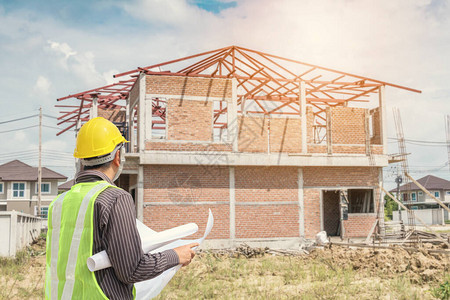 房屋建筑工地背景下带防护头盔和蓝图纸的专业图片