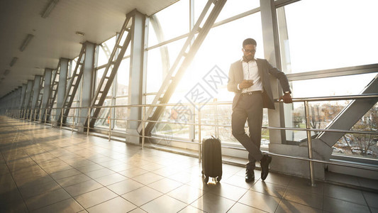 黑人企业家利用移动电话在机场航站楼等待飞行的旅行衣物图片