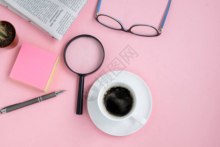 平躺在咖啡杯眼镜放大镜仙人掌钢笔和晨报的粉红色背景上图片