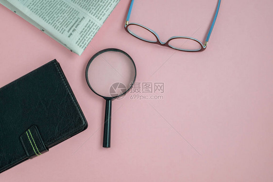平躺在粉色背景的眼镜放大镜小工具和晨报上图片