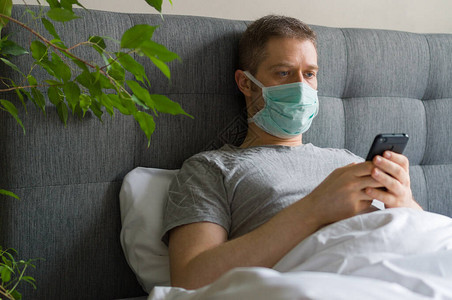 用手机在床上戴医疗面罩的病人家庭隔离概念图片