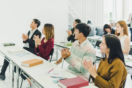 亚洲人参加研讨会并在培训室聆听演讲者的演讲有些人会记笔有人举手询问解说员并在演讲背景图片