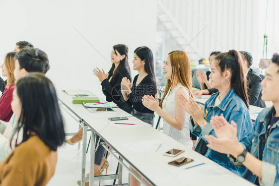 亚洲人参加研讨会并在培训室聆听演讲者的演讲有些人会记笔有人举手询问解说员并在演讲图片