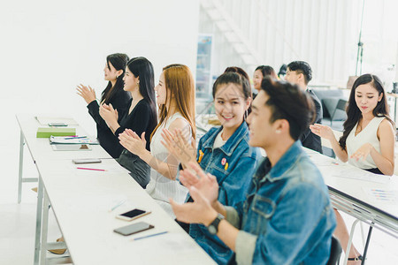 亚洲人参加研讨会并在培训室聆听演讲者的演讲有些人会记笔有人举手询问解说员并在演讲图片