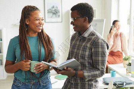 当代非洲裔美国女站在办公室时与同事交谈并愉快地微笑的腰部肖图片