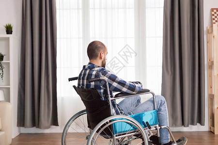 年轻人沮丧地坐在家里窗户附近的轮椅上图片