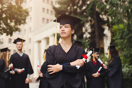 年轻严肃的女人在大学毕业那天与多民族学生站在一起教育资图片