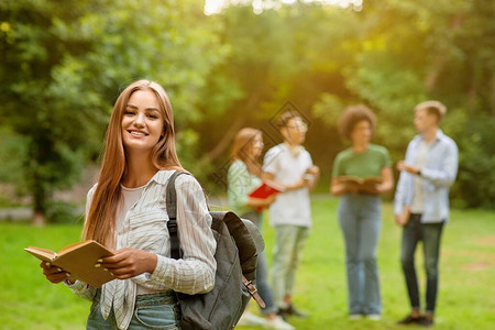 快乐微笑的女学生在大学校园里拿着书在户外摆姿势的肖像图片