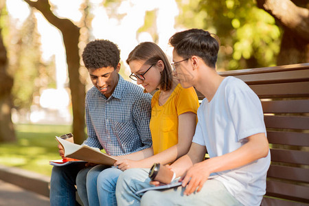 三名不同的学生坐在大学校园的户外长椅上图片