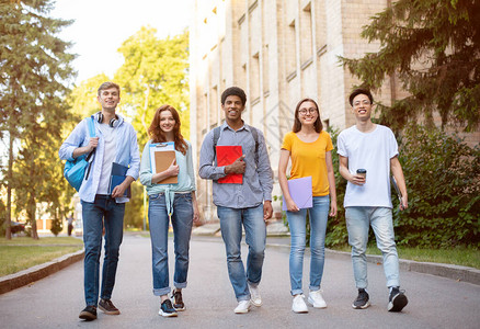 一群多种族的学生在外面的大学楼附近对着镜头微笑图片