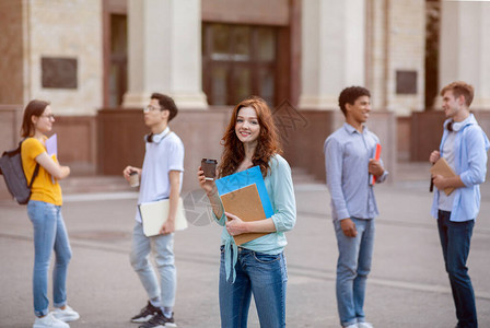 快乐的女学生在休息时喝咖啡站在大学楼外图片