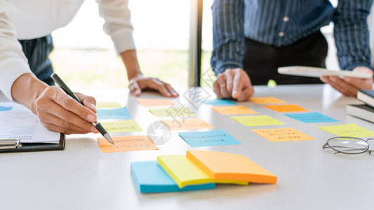 张贴粘笔记纸贴标签的年轻商业工人提醒同事在现代共同工作空间板上进行创造图片