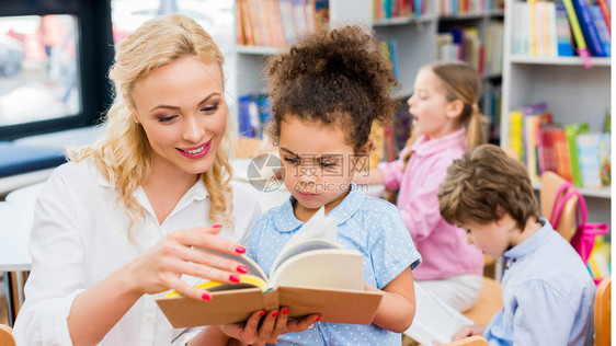 欢快的女子在可爱的非裔美国小孩身边读图片