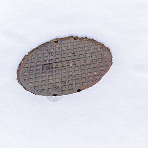 圆形和生锈的公用盖子在冬季被雪覆盖的地面所环绕图片