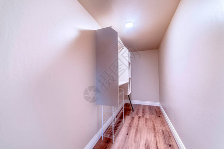 步入式壁橱与金属杆和壁挂式白色橱柜上的架子带棕色木地板和圆形吸顶灯的图片