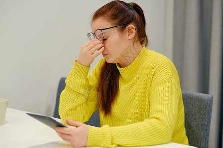 戴眼镜和针织毛衣的年轻白人女在阅读电子书时做鼻子按摩头痛压力血压问题图片