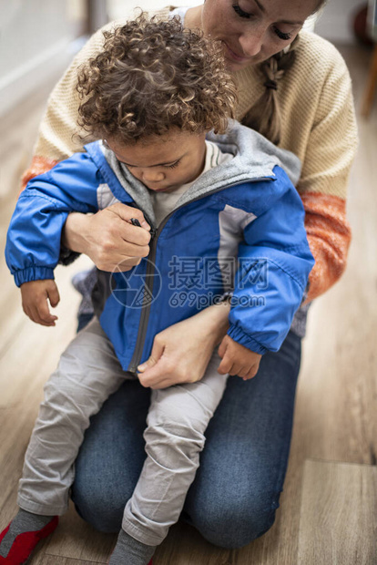 儿童照顾工作者给一个可爱的年轻的双种族儿童穿上夹克图片