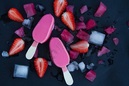 两块美味的粉红色冰淇淋黑色背景在切片草莓和切冰边旁图片