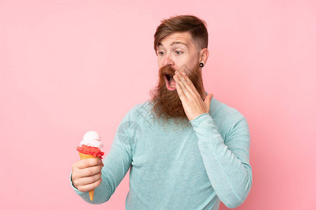 留着长胡子的红发男子在孤立的粉红色背景上拿着短号冰淇淋图片