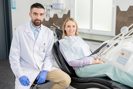 戴手套和白外套的年轻专业牙医和他的金发女病人图片