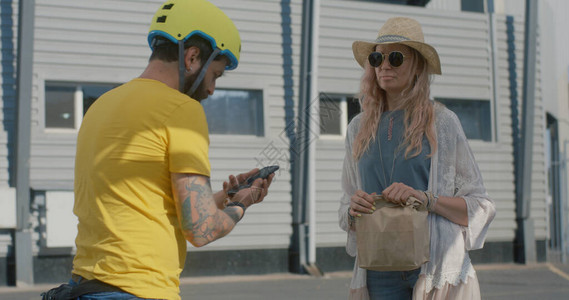中度自行车送信员向站在街上和电话聊天的妇女提供食物图片