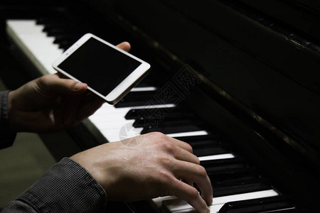 两只男手用智能手机在钢琴上图片