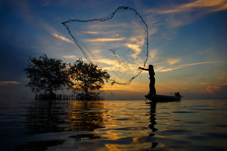 在泰国日落时丢渔网的鱼人休威特Silhou图片