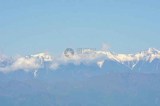 富士山的圆锥体在湛蓝的天空中升起一些薄雾从山的一侧吹过在前景中可以看到几棵树的顶部在一侧可以看图片