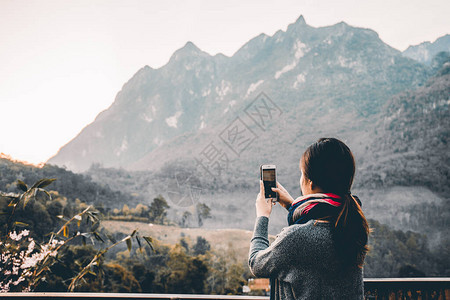 年轻女子用她的手机拍下美丽的山景照片图片
