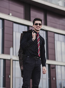 一个身穿黑衬衫和外套的年轻成功男子站在办公室外图片