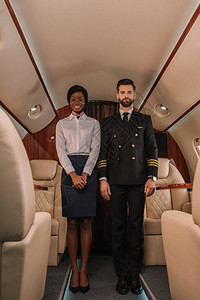 英俊自信有自信的驾驶员和微笑着容的美籍非洲空姐在私人飞机图片