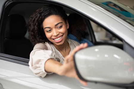 汽车所有权调整镜子的黑人妇女与丈夫坐在汽车经销店的汽车测试车中图片