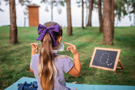 回到学校的新常态大流行现实中露天课后坐在草地上戴口罩的小学女生混合教育社交距离规则图片