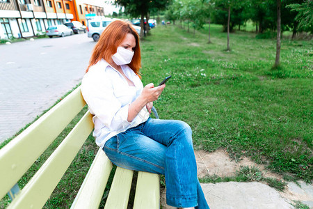 身戴面罩的女童坐在公园里使用手机图片