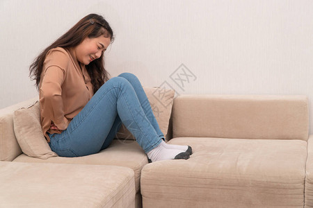 坐在沙发上并抱着胃痛月经的腹部不耐图片素材