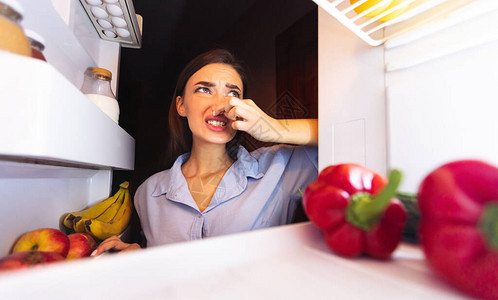 在冰箱附近闭着鼻子的年轻女人感觉臭味图片