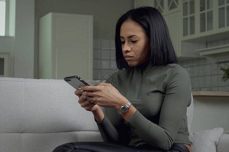 时尚的年轻非洲裔美国女肖像专注于在家中坐在沙发上使用手机漂亮的黑人女在家用智能图片