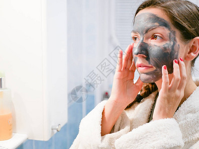 这个女孩正在照顾脸化妆品黑色面具一个女人给她的脸带来美丽图片