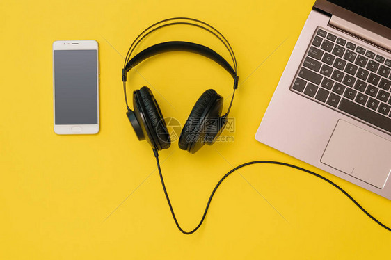 黄色背景上的智能手机耳机和笔记本电脑工作场所组织的概念用于录音交流和图片