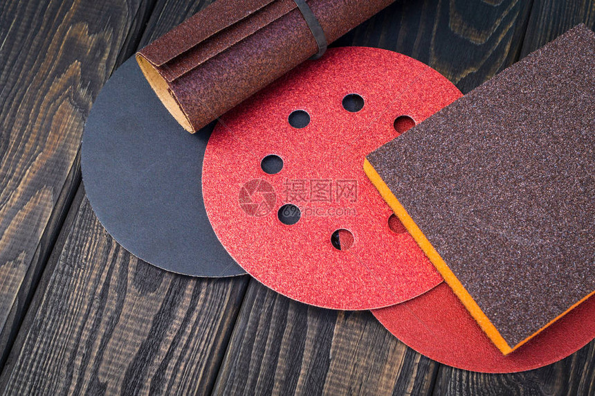 一套不同颜色的研磨工具和黑色复古木制背景上的砂纸该向导图片